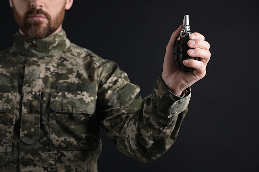 Soldier holding hand grenade on black background, closeup. Military service