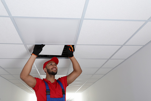 Electrician with pliers repairing ceiling light indoors, space for text