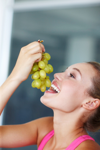 Pretty young girl eating a bunch of grapes with a smile