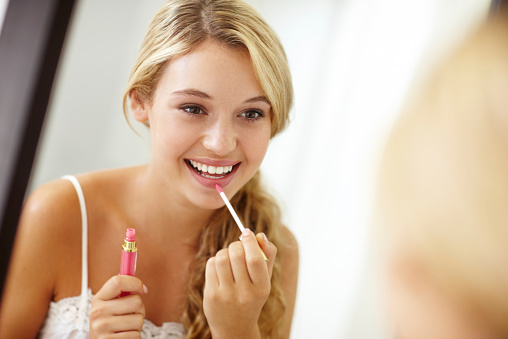 Lovely young woman applying lipgloss in front of a mirror