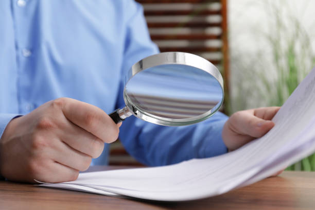 istock Man looking at document through magnifier at wooden table, closeup. Searching concept 1754819997