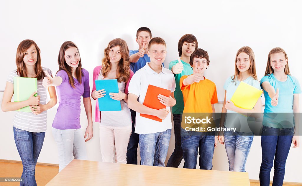 A group of cheerful preteen students with folders smiling  Group of cheerful preteen students next whiteboard with books and showing ok sign. 10-11 Years Stock Photo
