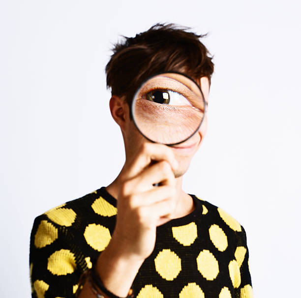 istock Young man looks through magnifying glass showing one huge eye 175482956