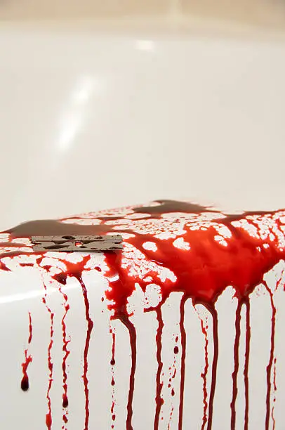 A razorblade sitting on the ledge of a bathtub surrounded by blood giving the appearance of a suicide.