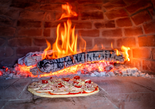 Uncooked italian pizza is cooking in a wood-fired oven