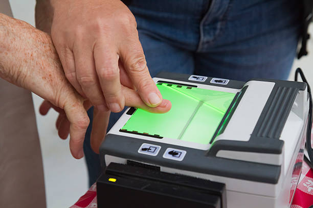 Man guiding another in using a fingerprint scanner stock photo