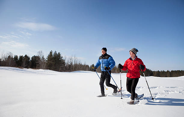 uomo e donna con le racchette da neve su un soleggiato giorno d'inverno. - snowshoeing foto e immagini stock