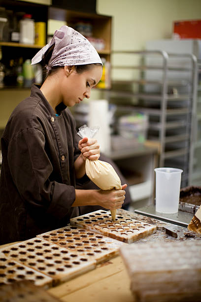 A woman makes chocolate bonbons in an industrial kitchen Young chef filling chocolate shells in chocolate mold. Selective focus. chocolate truffle making stock pictures, royalty-free photos & images