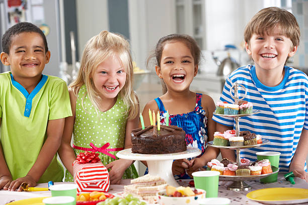 Children Standing By Table Laid With Birthday Party Foo