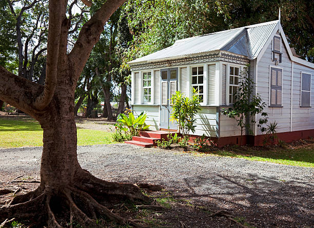 A typical traditional small house in Barbados. Wooden construction with a metal roof. A large tree provides welcome shade in the front yard.