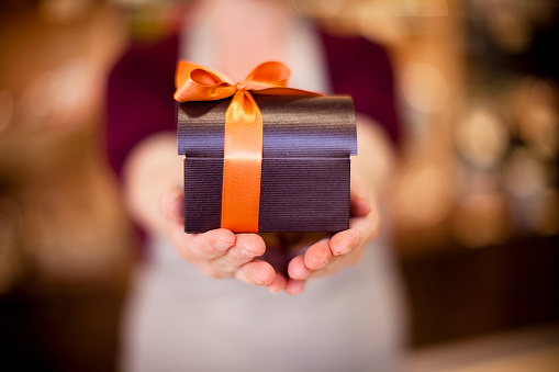 Sales person offering a wrapped chocolate box. Selective focus.