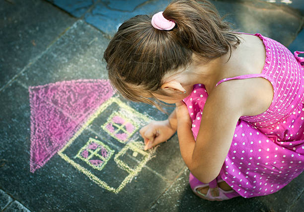 Adorable toddler girl drawing with colorful chalks on asphalt. Outdoor activity and creative games for small kids