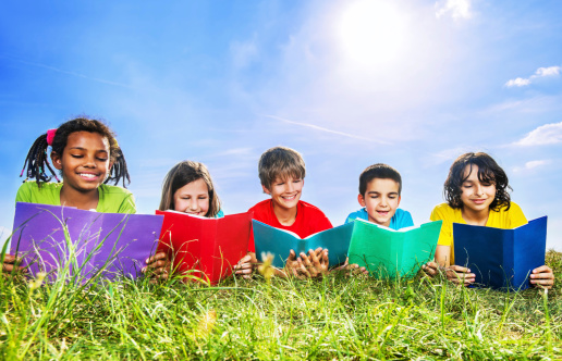 Cheerful kids lying in the park against the sky and reading books.