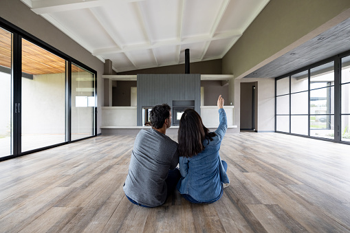 Happy Latin American couple moving to their new house and sitting on the floor thinking about decoration ideas - home ownership concepts
