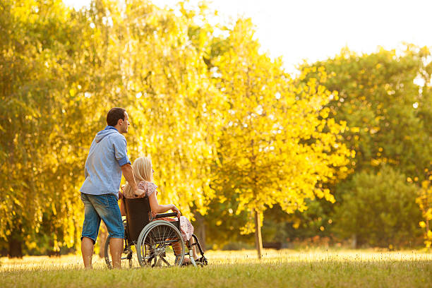 Handicapped Couple Outdoors. "Portrait of an young couple, man and disabled woman in wheelchair walking in a park." long stock pictures, royalty-free photos & images