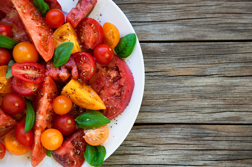 Heirloom tomato and basil salad on a rustic wood background.