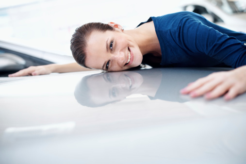 Young woman laying her head on the bonnet of her new vehicle