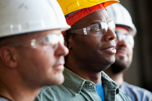 Close up of group of multi-ethnic construction workers wearing hard hats and safety glasses.  Focus on African American man (30s).