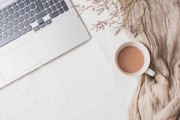 istock Coffee cup, laptop computer and small kermek flowers on white linen. Cozy workplace, breakfast, comfort, hygge concept. Top view, flat lay 1754902467