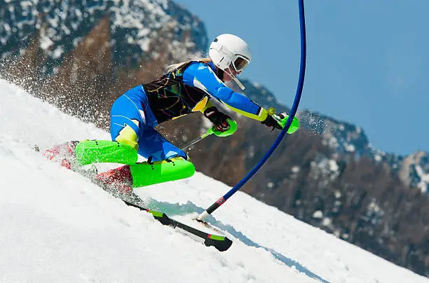 Side view of young female skier hitting the blue gate during slalom ski race