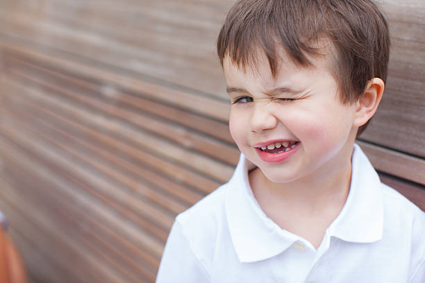 Cheerful boy looking at his first lost bottom front milk tooth over grey background. Child dental health care concept.