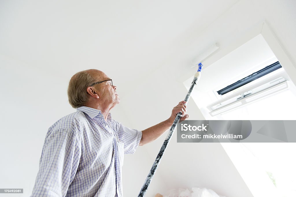 Active senior hombre está pintando un muro en su hogar. - Foto de stock de 60-69 años libre de derechos