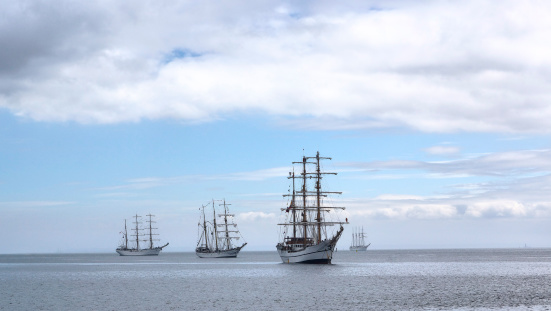 Fleet of sailing ships at anchor in late afternoon.