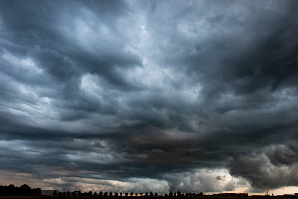 Stormy cloudy sky dramatic dangerous dark gray cloudscape Sinister skyscape above tiny silhouette of treesPLEASE SEE ALSO: dramatic sky stock pictures, royalty-free photos & images