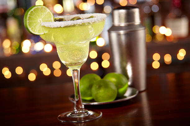 Margarita at a bar A margarita in a traditional glass on a dark wood surface with a bar in the background tequila drink stock pictures, royalty-free photos & images