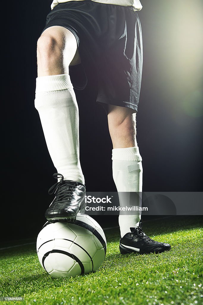 Football player ready to kick ball Close up of the legs of a soccer player at night at a stadium. He has one foot on the ball. Note: a bit lens flare. Soccer Stock Photo