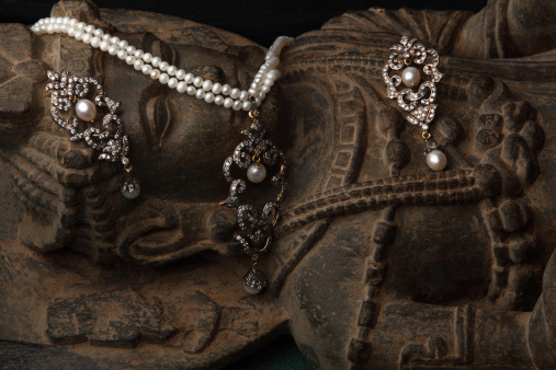 Crystals and pearl earring and Pendant with crystal string over statue of ancient Buddha from Gandhara in Pakistan.