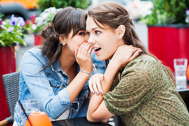 Two best friends sitting in a cafe and gossiping, Two female friends sitting in a sidewalk cafe. They are whispering and gossiping.    gossip photos stock pictures, royalty-free photos & images