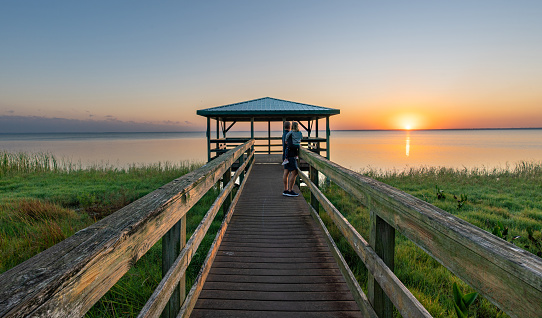 Father and daughter enjoying a vibrant sunrise over a boardwalk and dock at Lake Apopka near Orlando in Central Florida