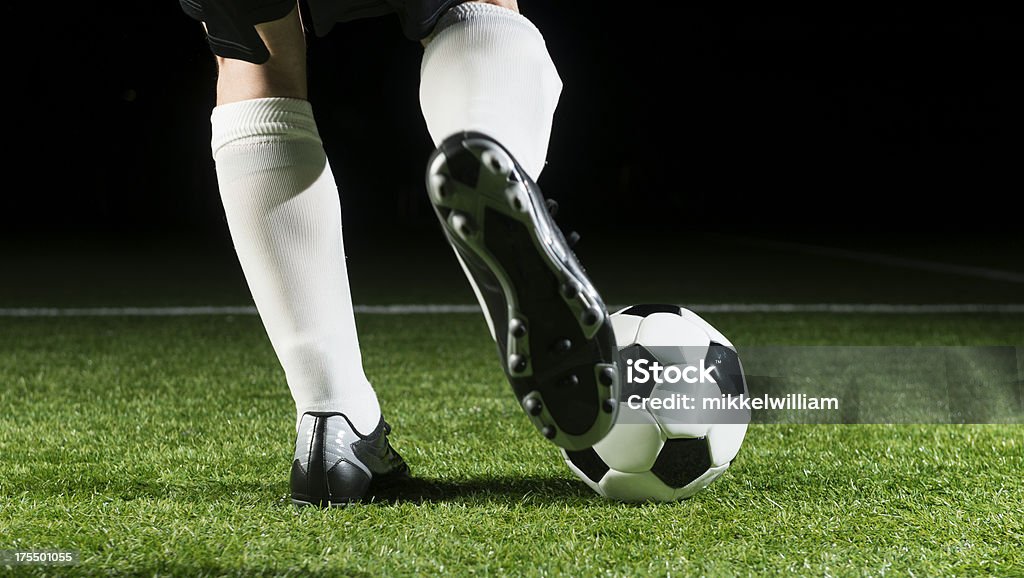 Soccer player is about to kick ball Close up of soccer play who is about to kick a soccer ball. The ball is on a beautiful soccer field (stadium) at night. Soccer Stock Photo