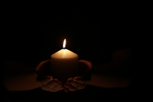Hope illuminates ,Hands holding a burning candle in the dark like a heart-shape