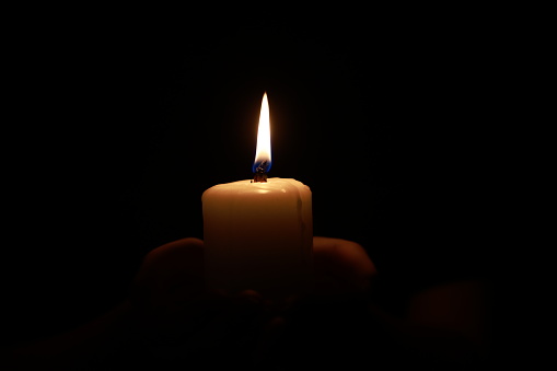 Hands holding a candle over dark background
