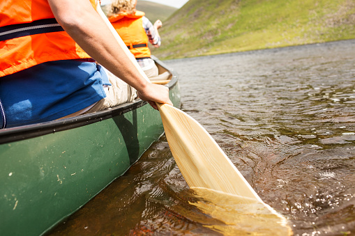 Cropped image of man rowing boat in a river with woman sitting in background. Horizontal shot.