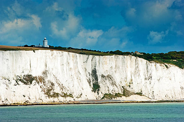 The white cliffs of Dover with a small, distant silhouette of a lone tourist standing on top of the cliff edge on a spring afternoon, United Kingdom.