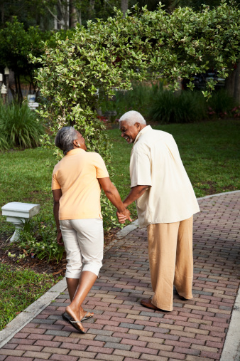Rear view of senior African American couple holding hands, walking through park.