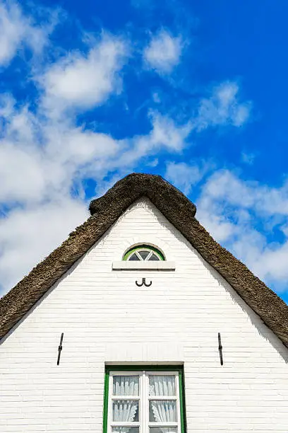 Home with traditional straw roof in front of a blue sky, with beautiful clouds