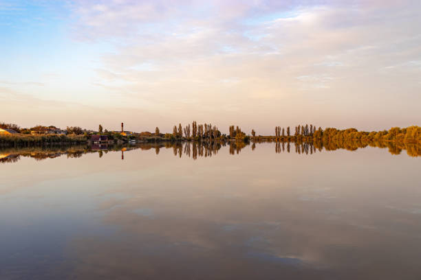 Picturesque shore of lake with pyramidal poplars, which are reflected in smooth surface of water. .