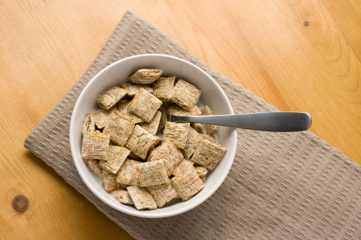 A bowl of bite-size shredded wheat on a wooden surface.