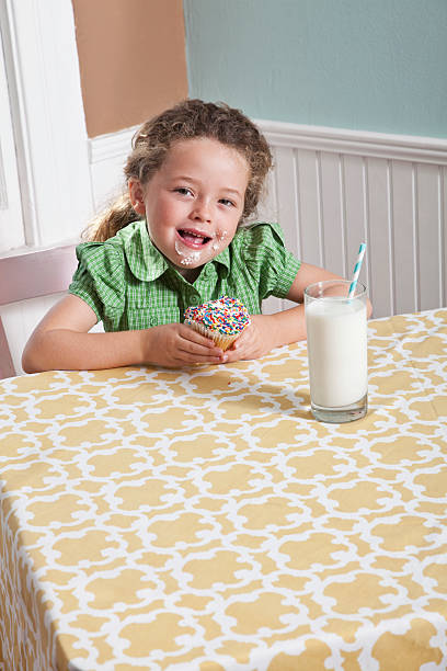 menina com um copo de leite comendo cupcake - sc0563 - fotografias e filmes do acervo