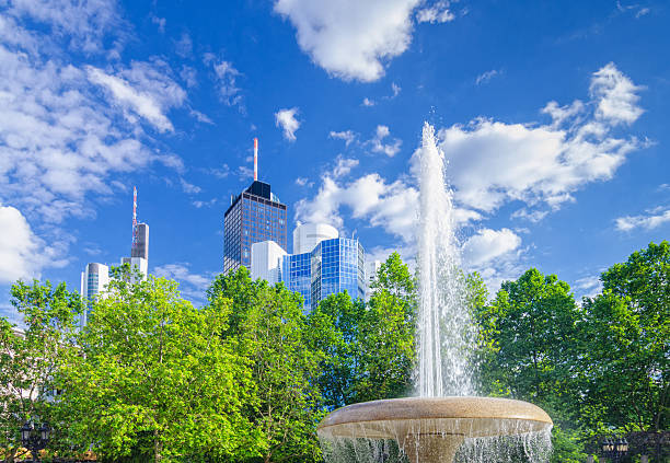 Opera Square (Opernplatz) timelapse hyperlapse in downtown Frankfurt, Germany, showcases a fountain with skyscrapers and towers in the background, surrounded by trees and city life under evening sky