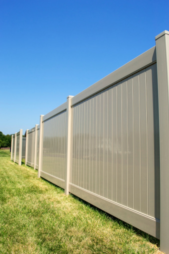 Tan vinyl fence running across a yard with blue sky in the background