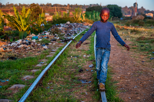 African little boy walking on railroad tracks, Kibera slum on the background, Kenya, East Africa. Kibera is the largest slum in Nairobi, the largest urban slum in Africa, and the third largest in the world