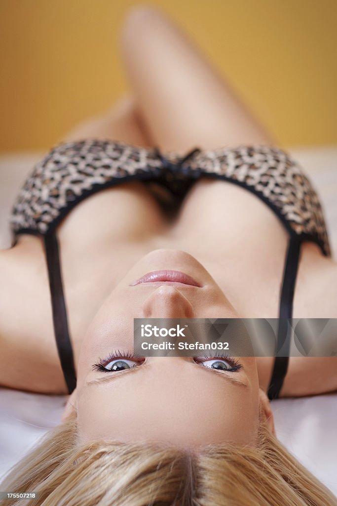 Blonde girl on bed Blonde girl lying on bed with white satin bedding. Adult Stock Photo