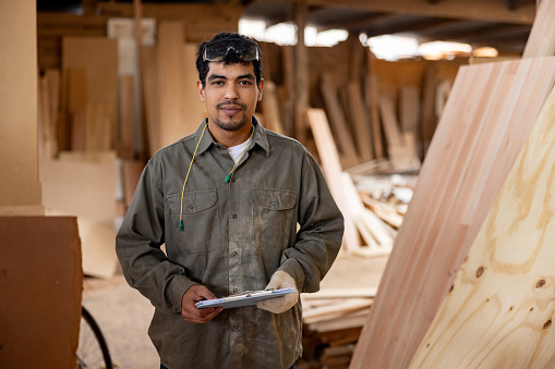 Latin American worker taking inventory of wood while working at a lumberyard and looking at the camera - people at work concepts