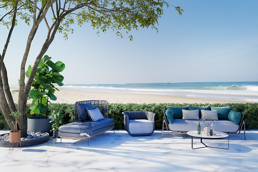 Patio with garden furniture overlooking empty beach in the summer. 3D generated image.