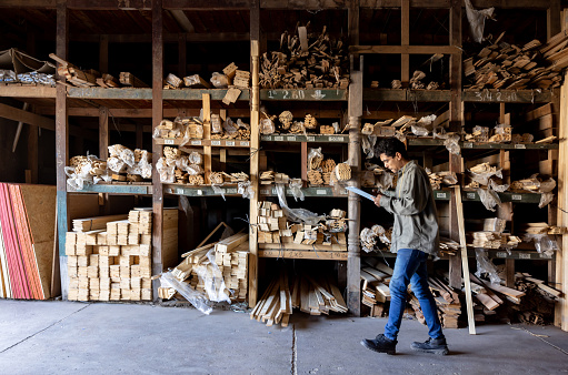 Latin American man working at a lumberyard taking inventory on logs of wood and writing on a clipboard